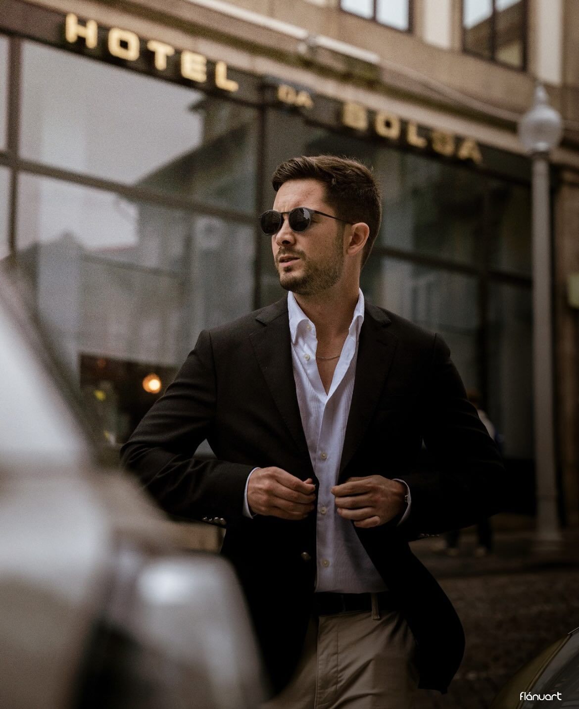 Stylish man in dark blazer adjusting jacket outside Hotel da Bolsa building.