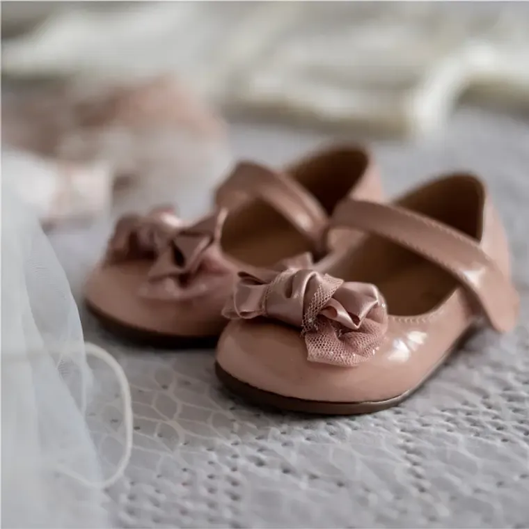 Pair of pink patent leather baby shoes with bow detail on soft fabric.