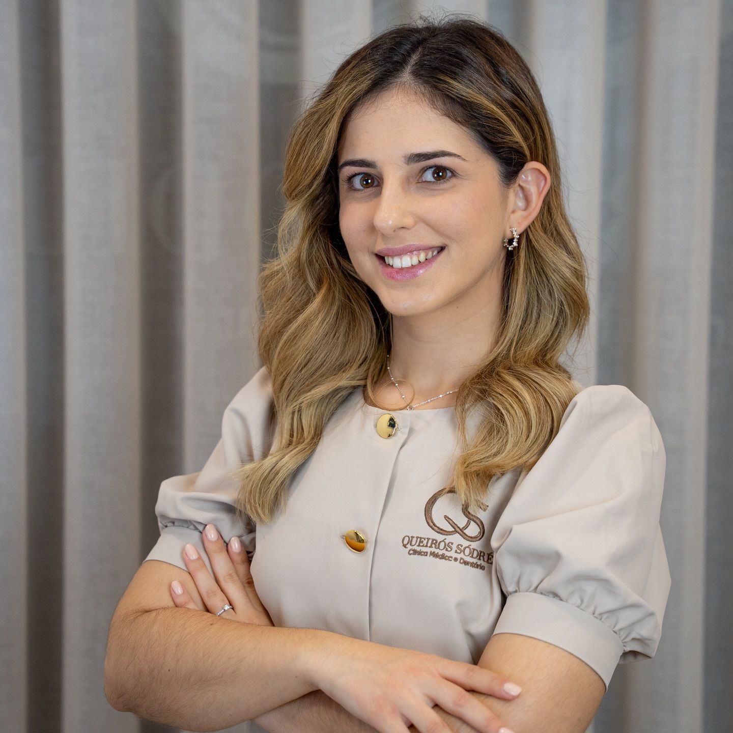 Smiling female healthcare professional in beige scrubs with crossed arms posing for a portrait photo.