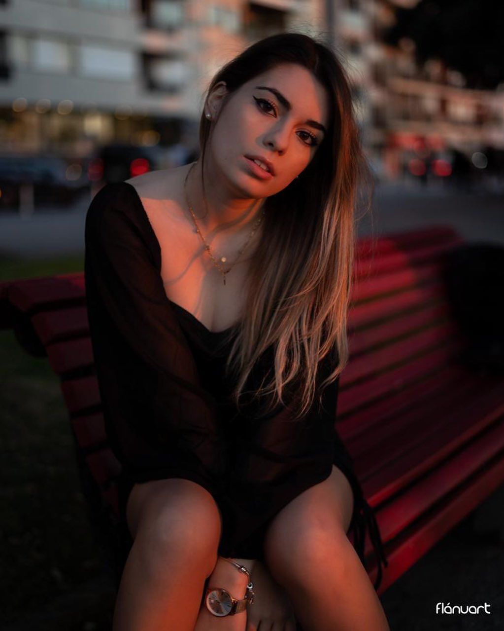 Young woman in black outfit sits on a red bench outdoors during golden hour light.