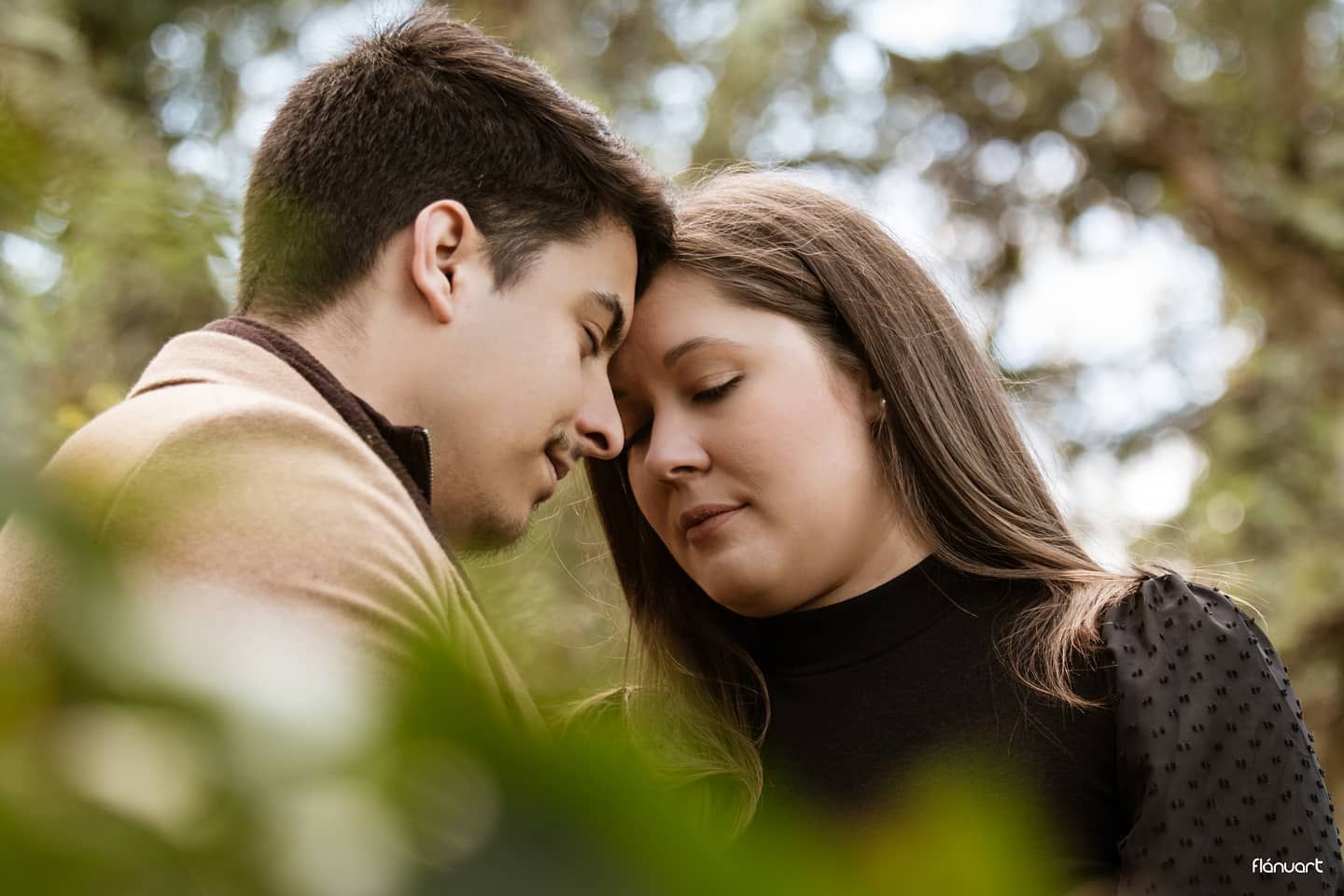 Young couple sharing a tender forehead-to-forehead moment outdoors surrounded by lush green foliage.