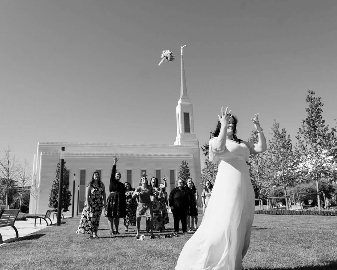 Bride tosses bouquet to excited guests outside a white church on a sunny wedding day.