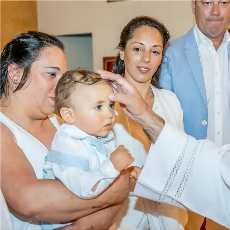 Baby boy being blessed by a priest during a baptism ceremony in a church.