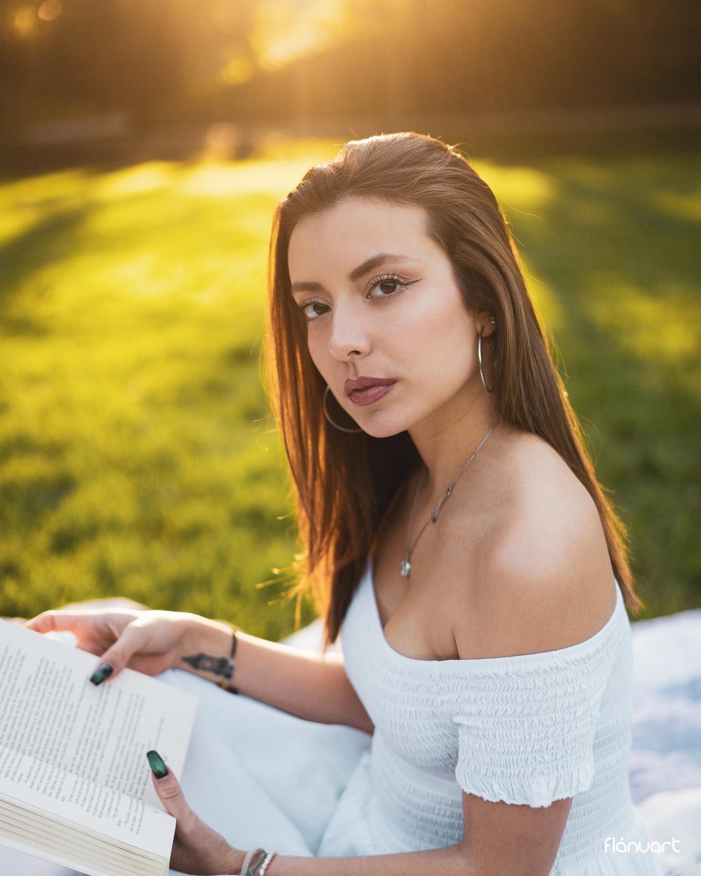Young woman in white off-shoulder top reading book in golden sunset light.