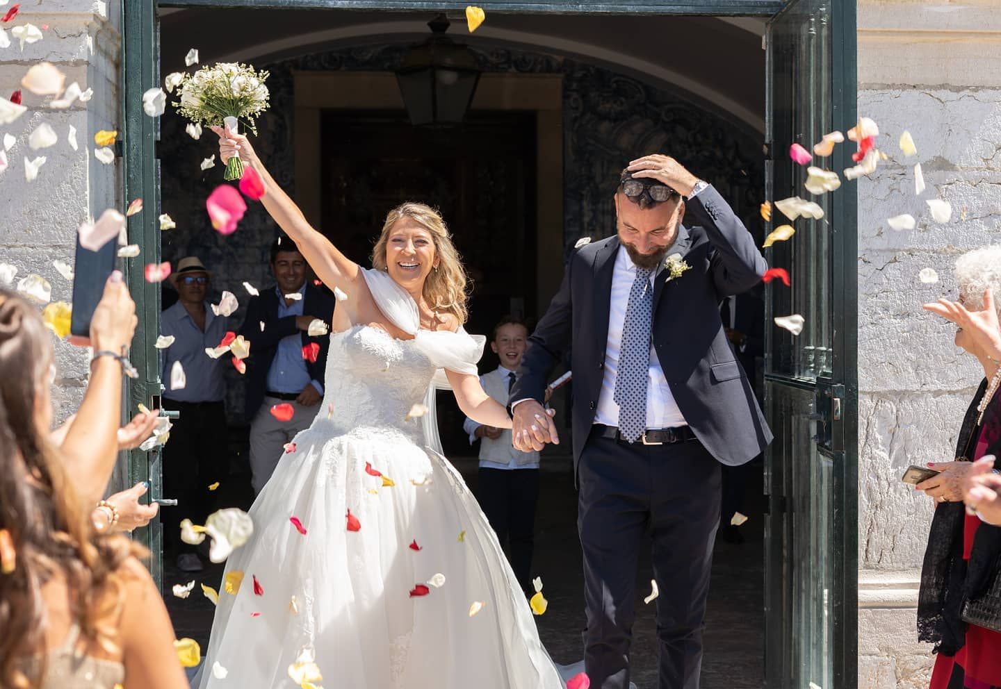 Newlyweds exit church celebrating with colorful confetti as guests cheer their marriage.