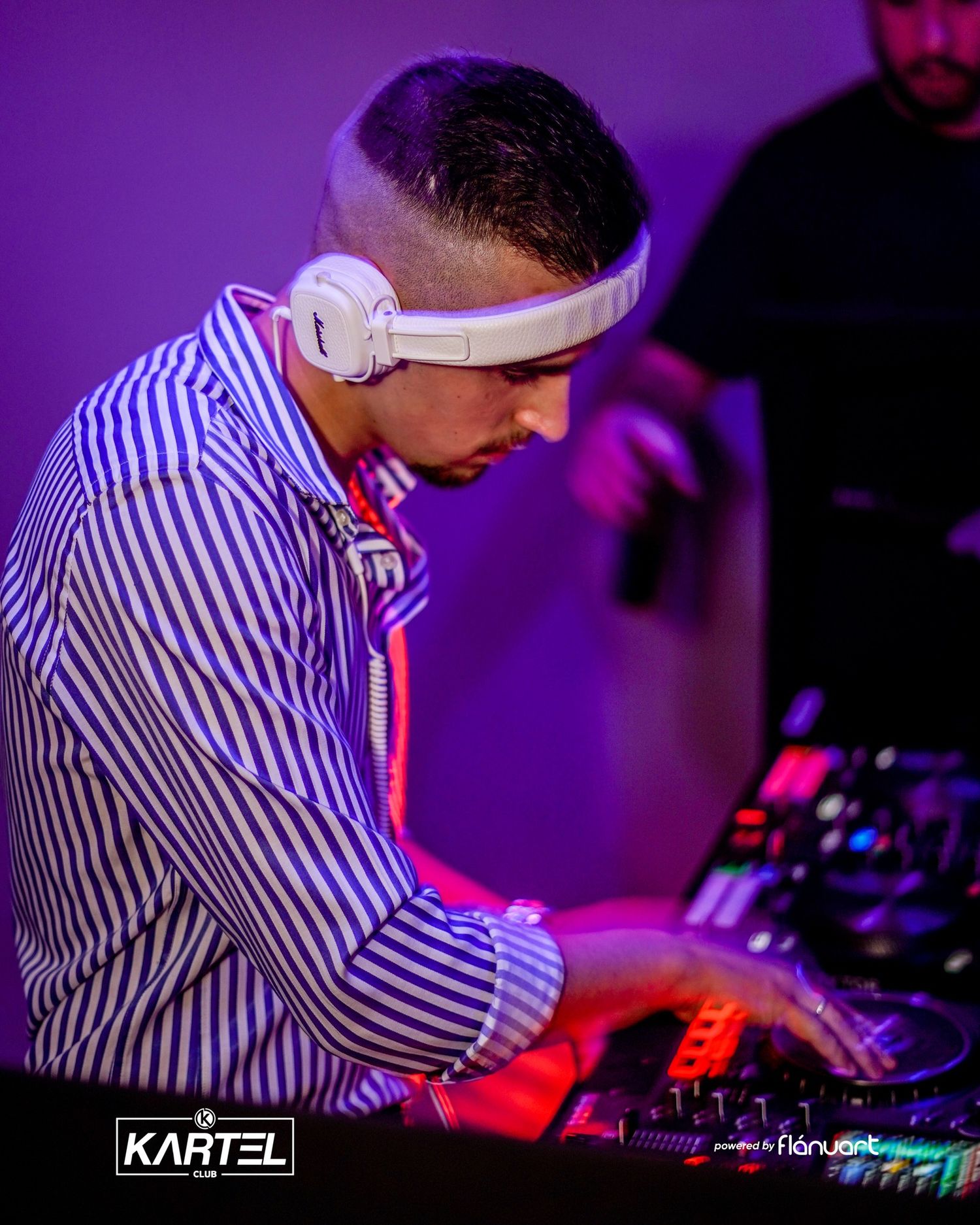 DJ wearing white headphones and striped shirt performing at Kartel Club nightclub event.