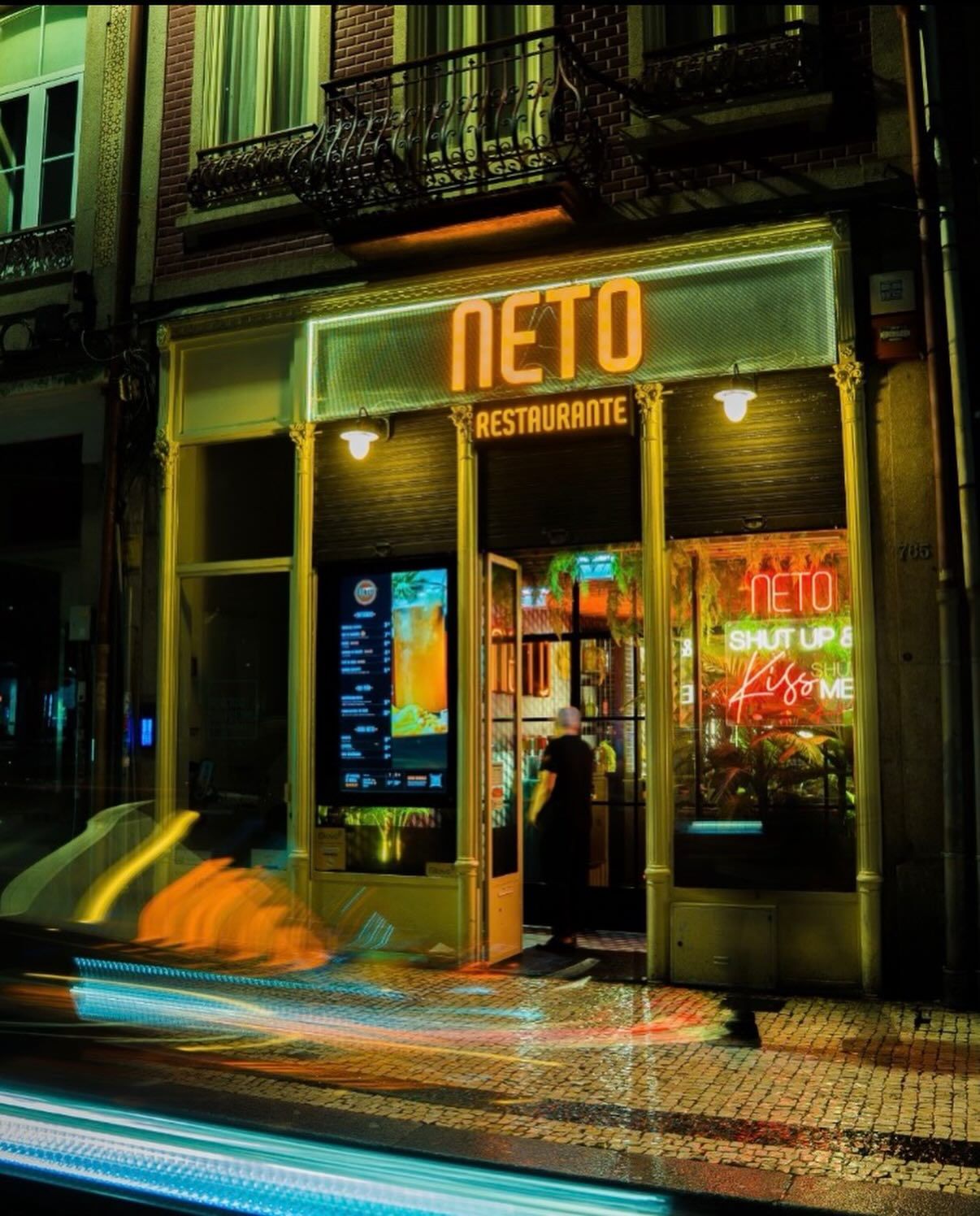 Neto Restaurante glowing neon storefront at night with colorful light trails on a city street.