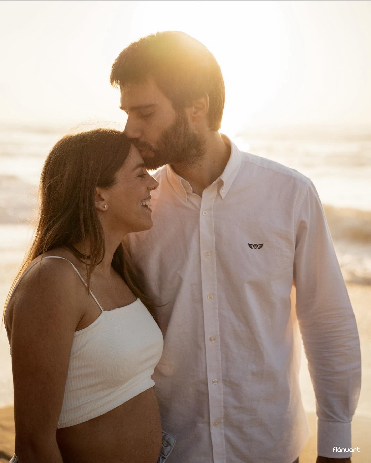 Romantic couple sharing a tender moment at sunset on a beach, man kissing woman's forehead.