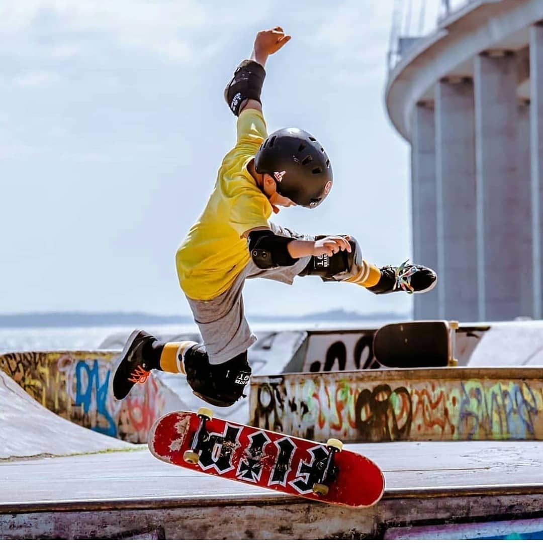 Young skateboarder in yellow jacket performing an aerial trick at an outdoor skate park.