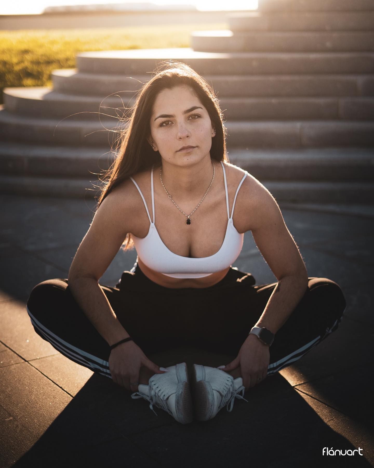 Athletic woman in white sports bra and black leggings stretches in seated pose at sunset.