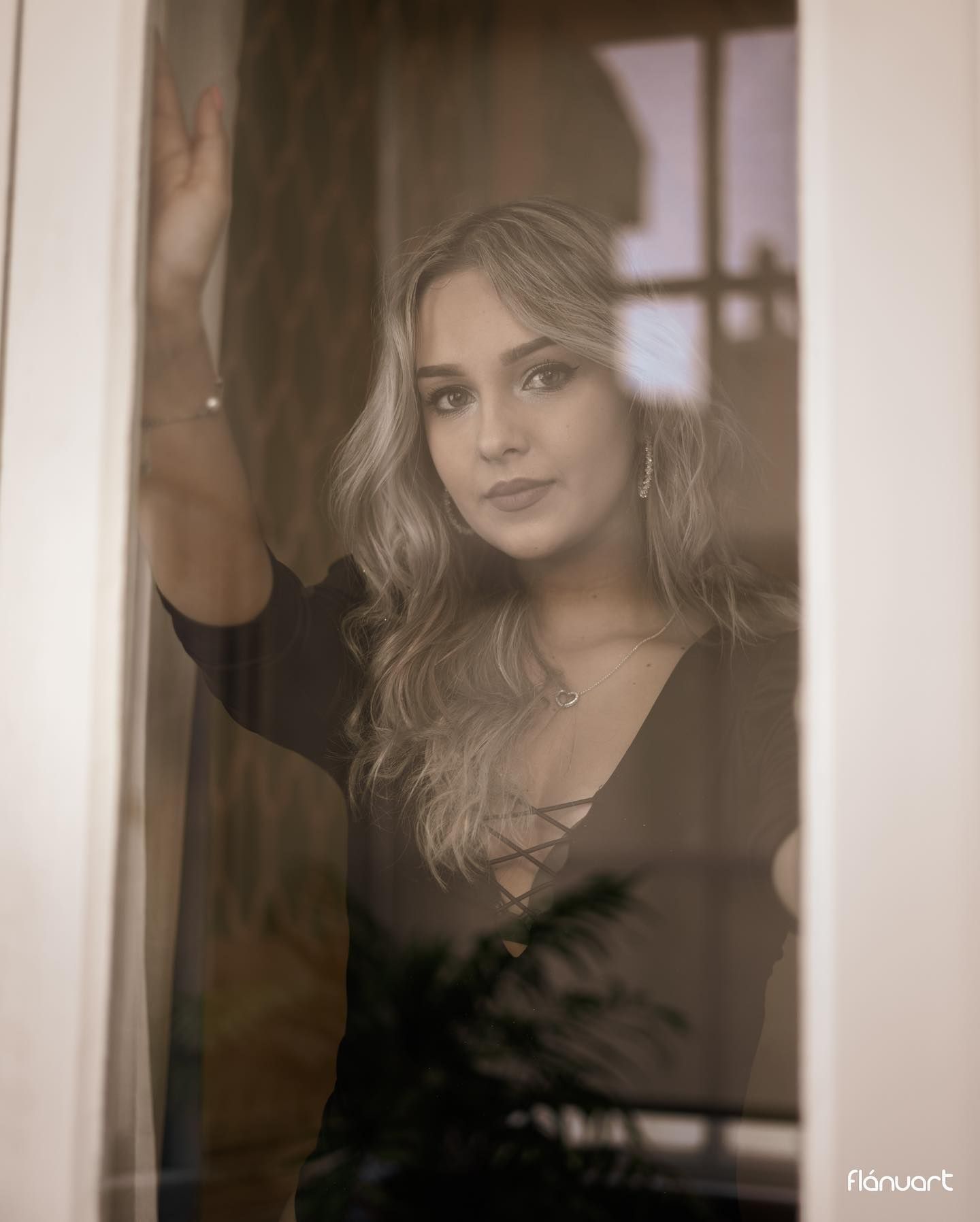 Blonde woman in black top gazing through a window in a moody, atmospheric portrait.