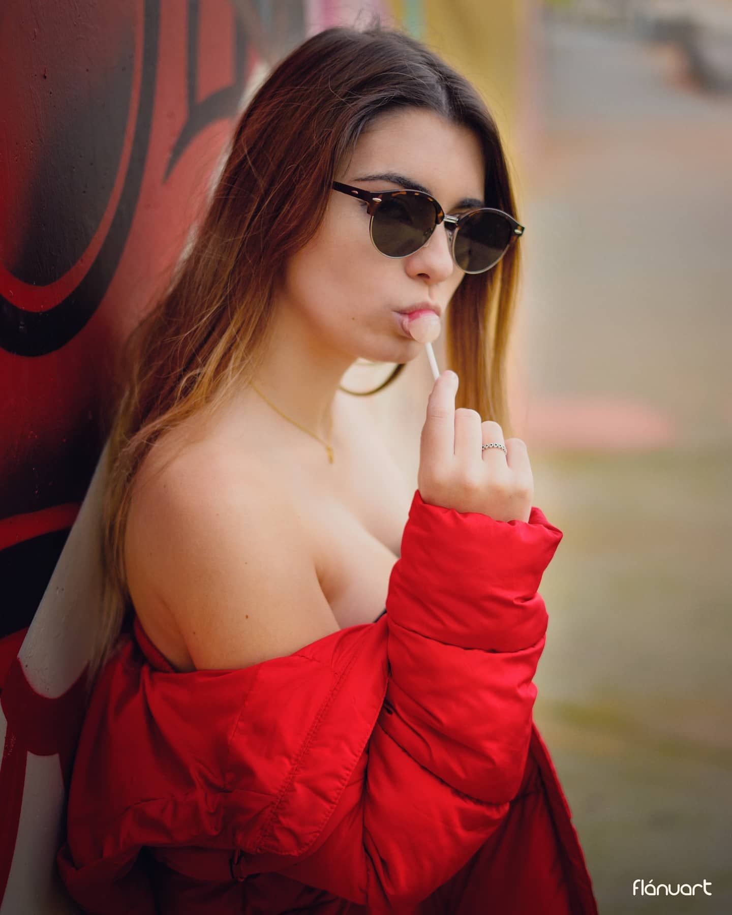 Woman in red off-shoulder jacket wearing sunglasses poses against a colorful graffiti wall.