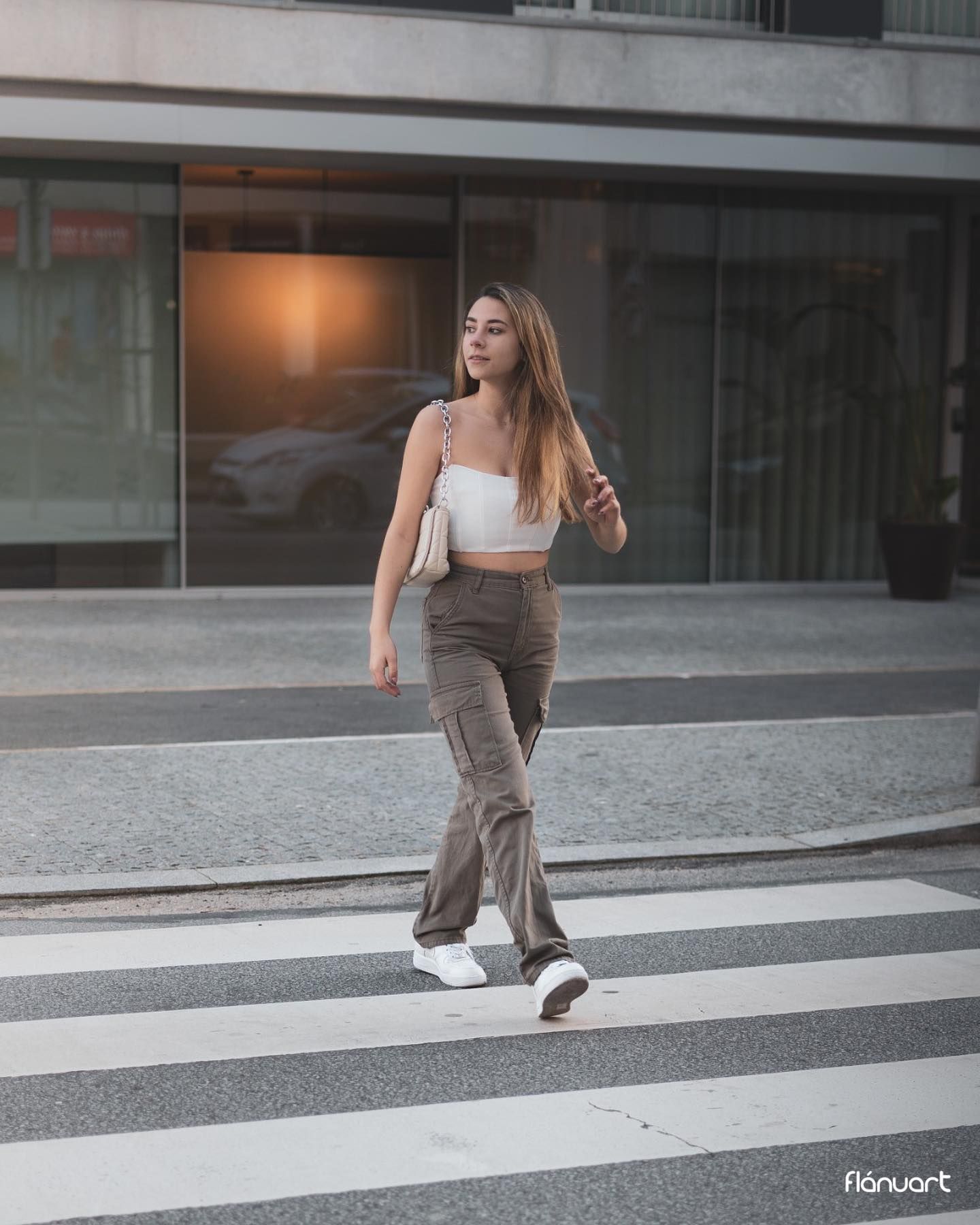 Stylish woman in white crop top and cargo pants walks across a zebra crossing in an urban setting.