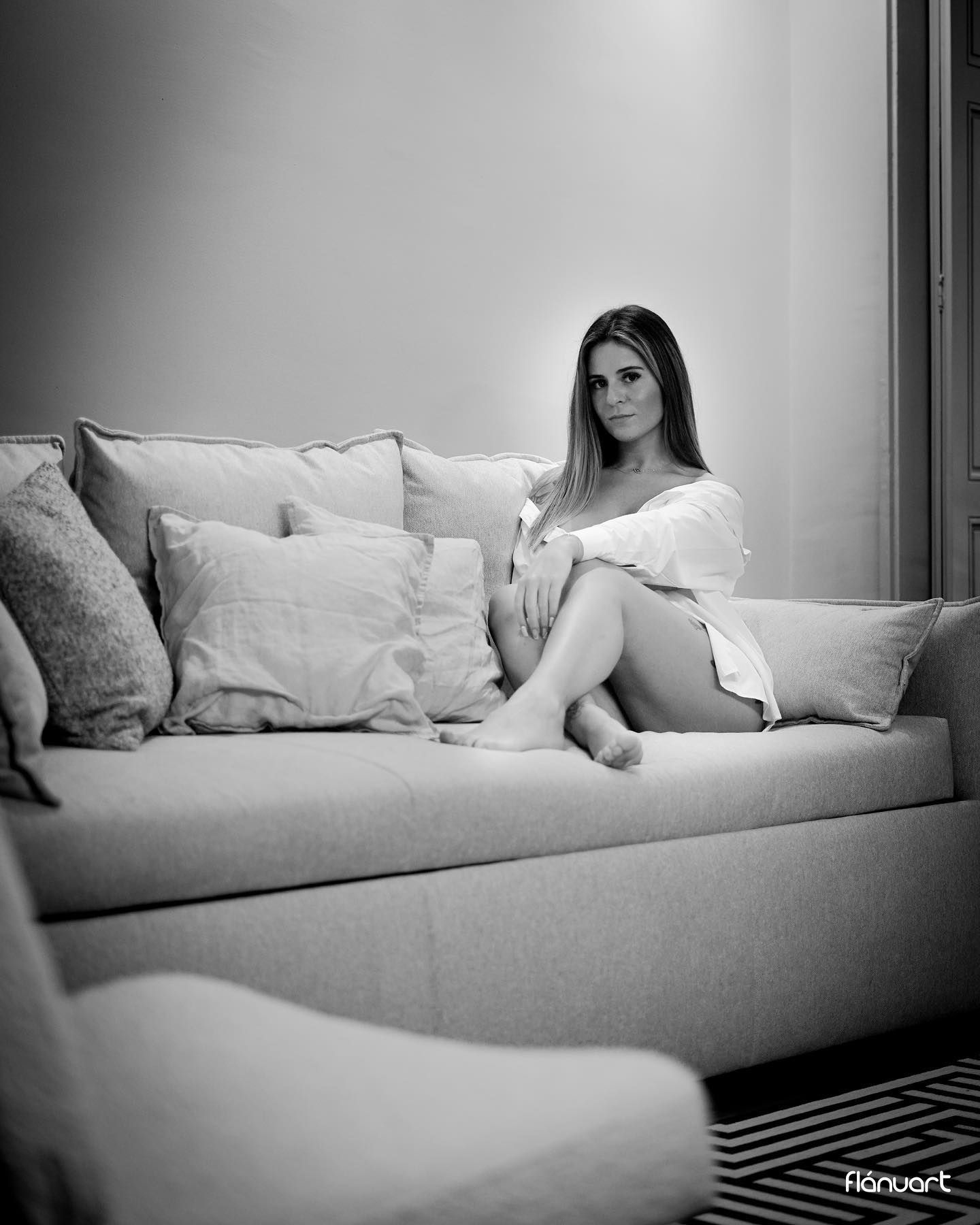 Black and white photo of a woman in a white outfit relaxing on a large sofa.