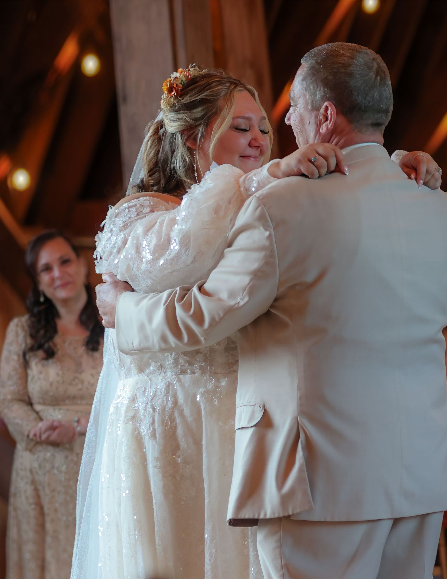 Emotional bride in lace wedding gown sharing first dance with father in barn wedding venue.