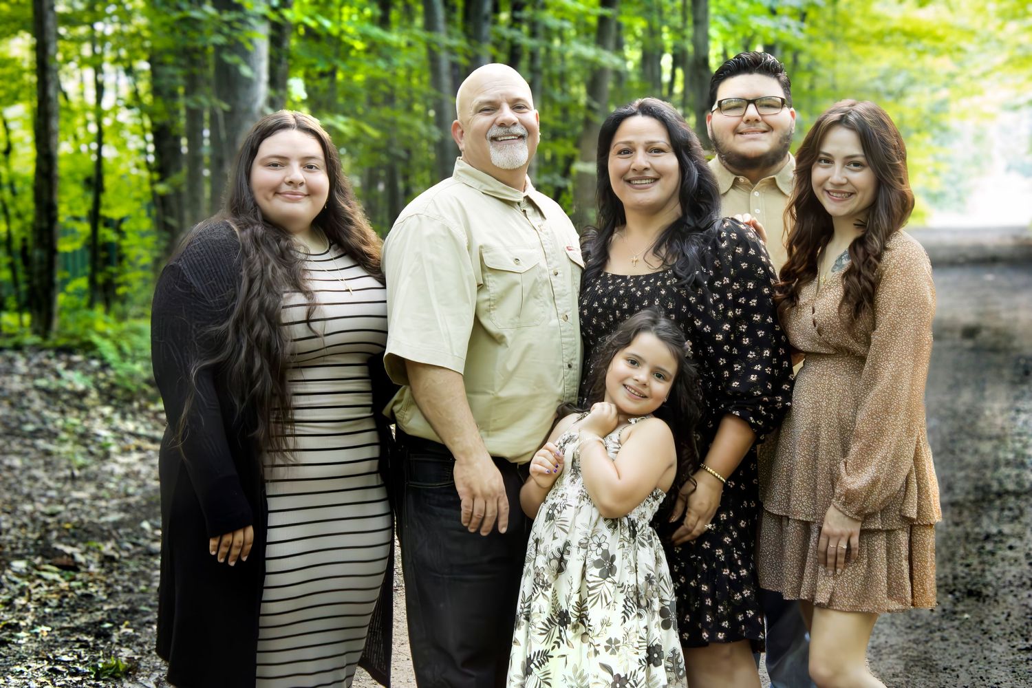 A joyful family of six poses together outdoors in a lush green forest setting, smiling warmly for a portrait.