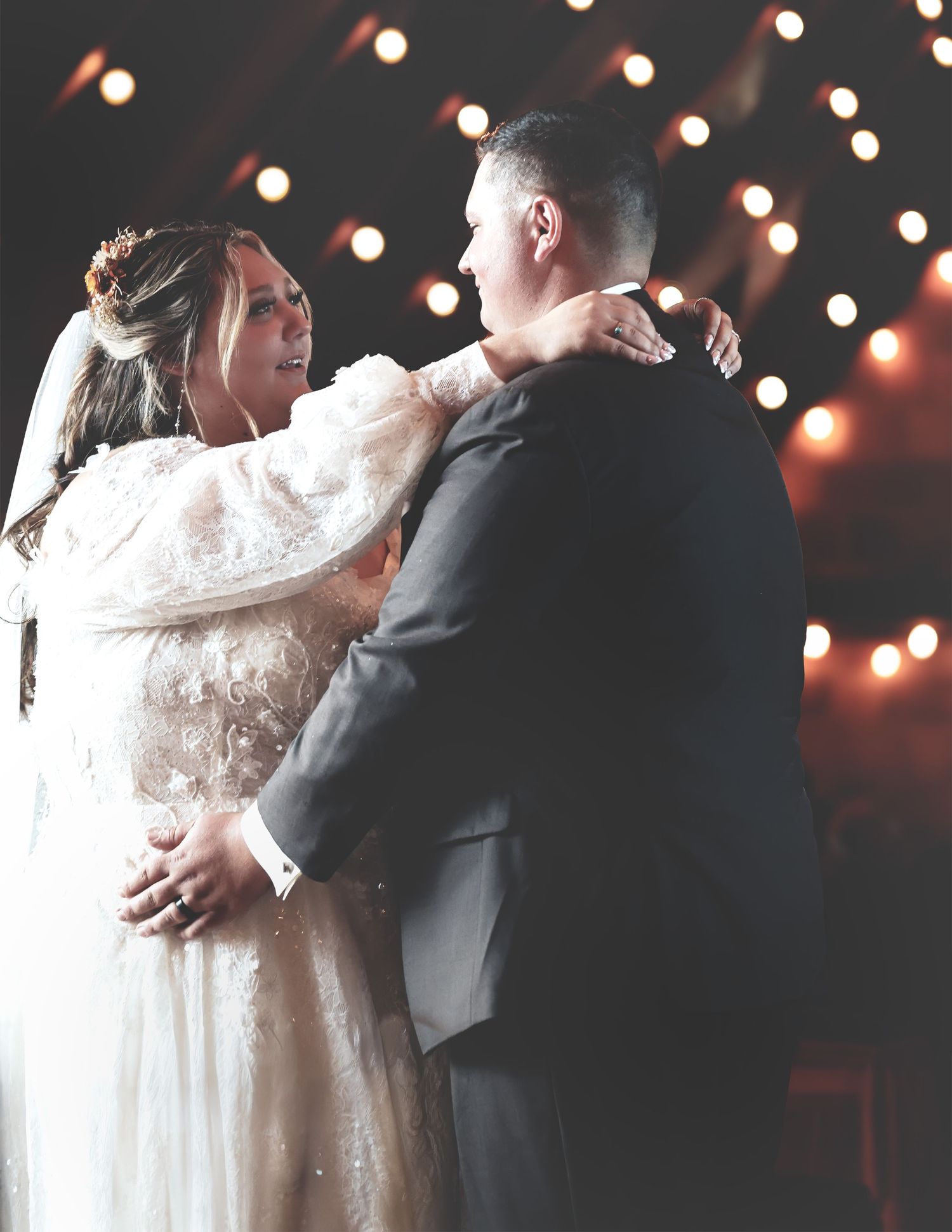 Bride and groom sharing first dance at romantic wedding reception with string lights.