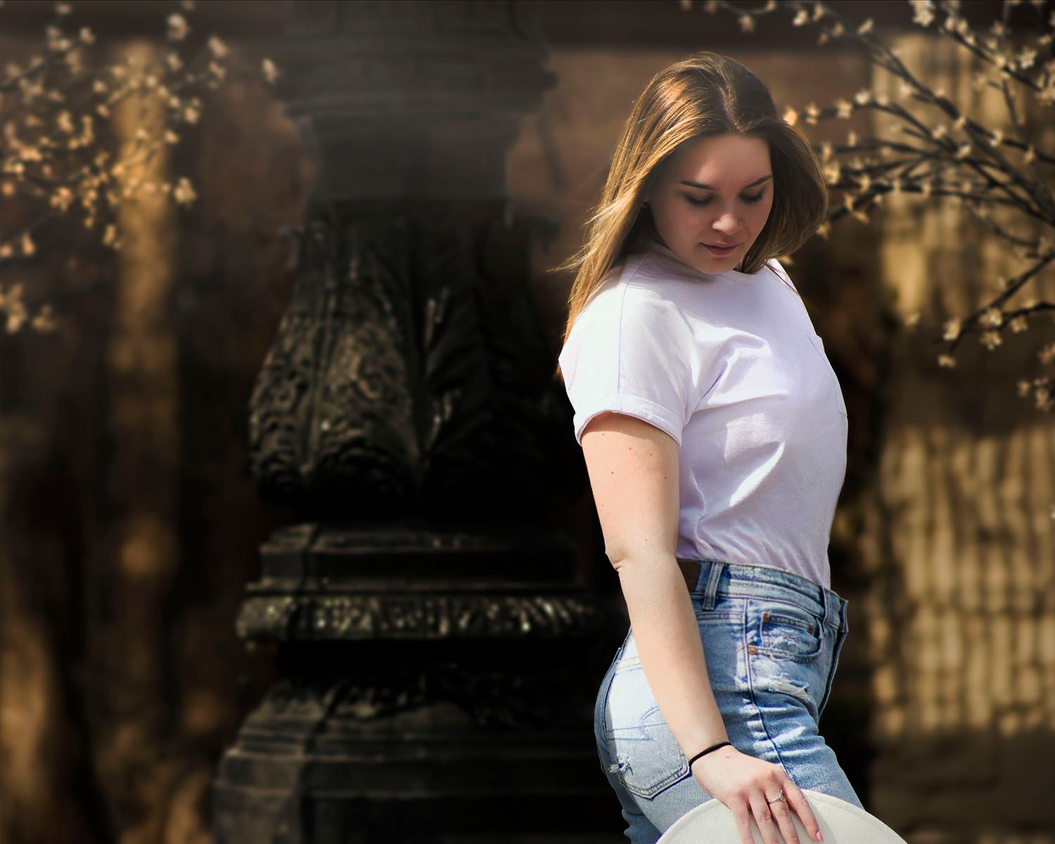 Young woman in white t-shirt and ripped jeans leaning against ornate dark stone column.