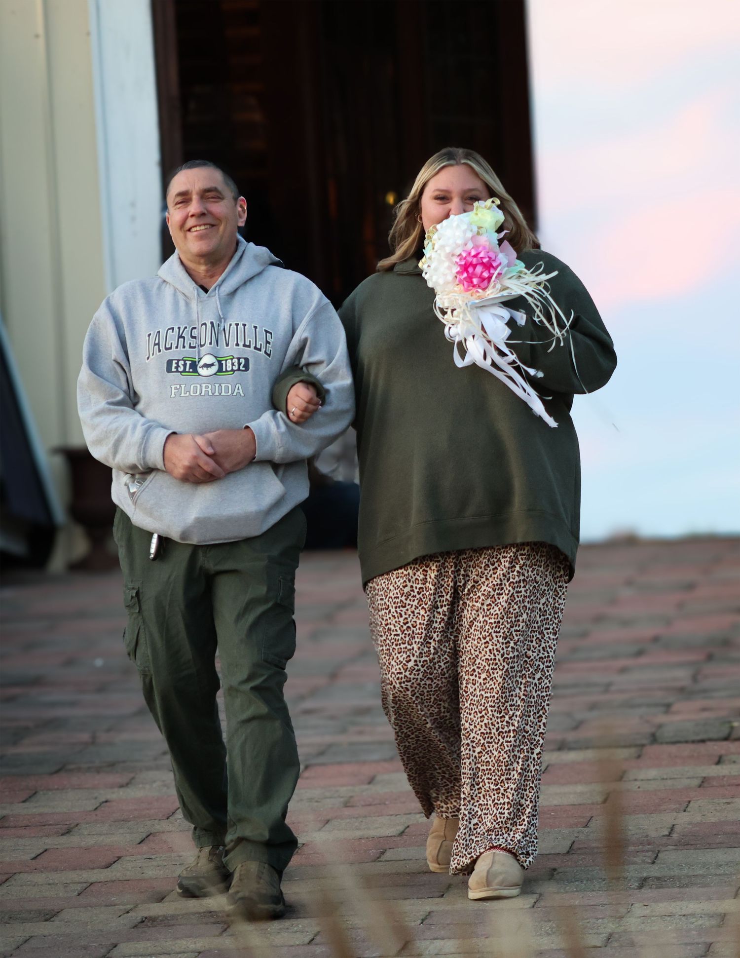 A man in a Jacksonville Florida hoodie walks alongside a woman holding a bouquet of flowers outside a building.