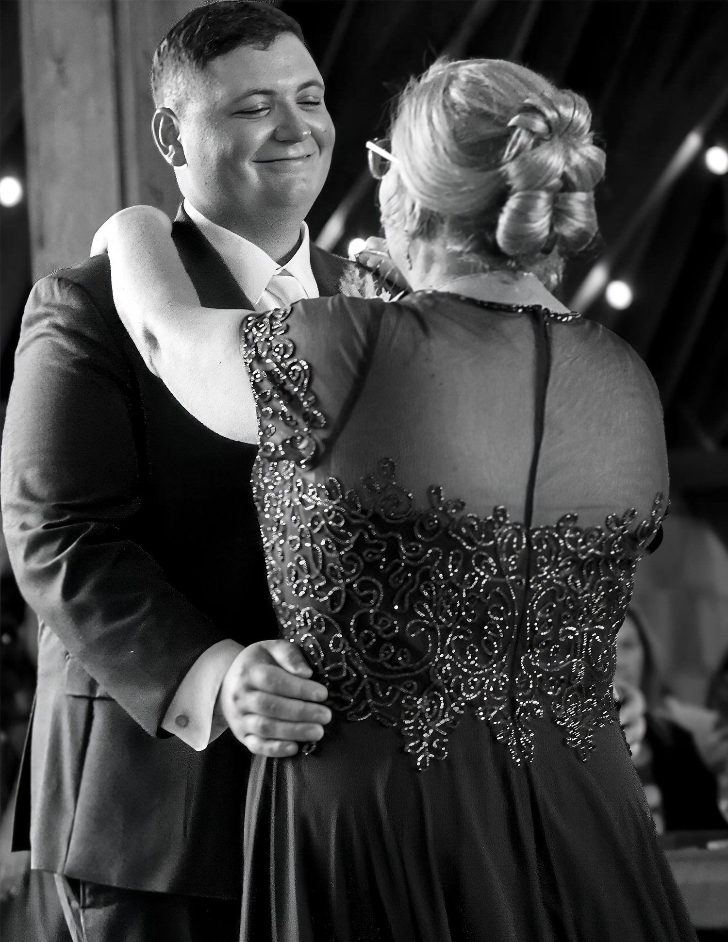 Groom dancing with woman in elegant embroidered gown at wedding reception.
