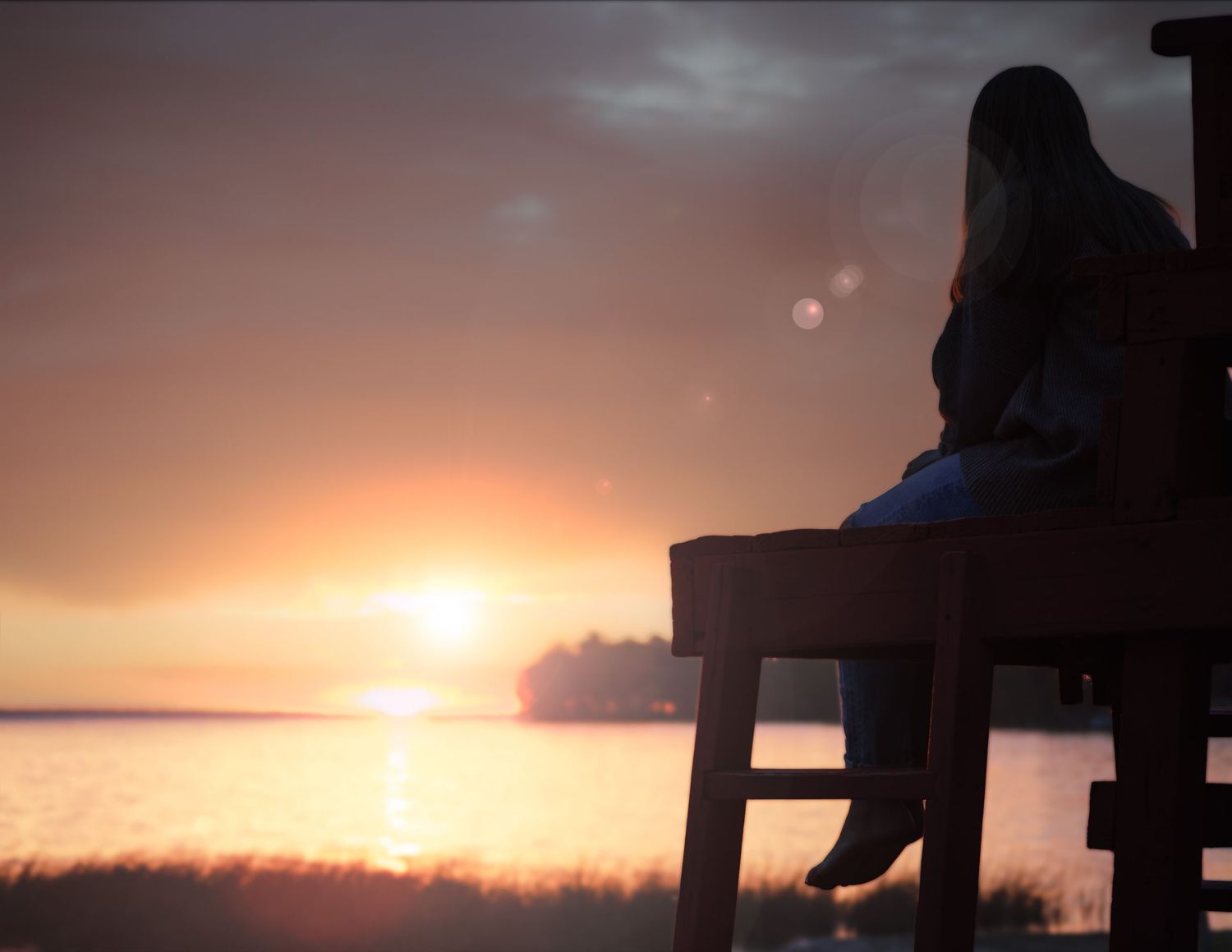 Silhouette of a person sitting on a wooden chair watching a vibrant sunset over water.