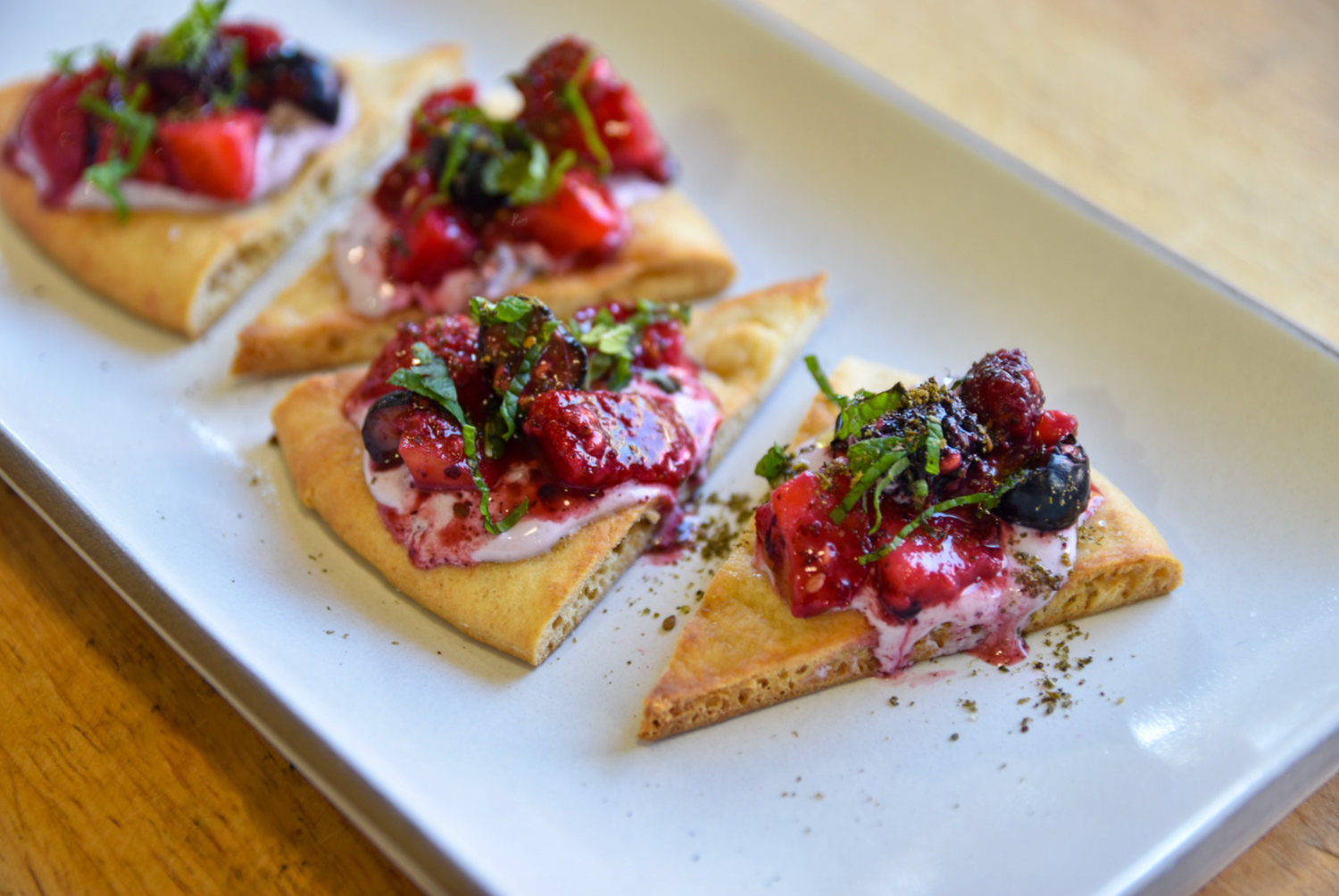 Three pieces of crispy flatbread topped with fresh mixed berries, cream, and chopped mint herbs.