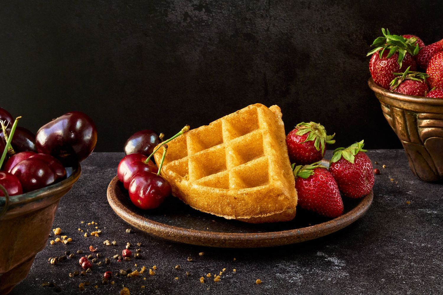 Golden waffles served on a rustic plate with fresh strawberries and cherries on a dark background.