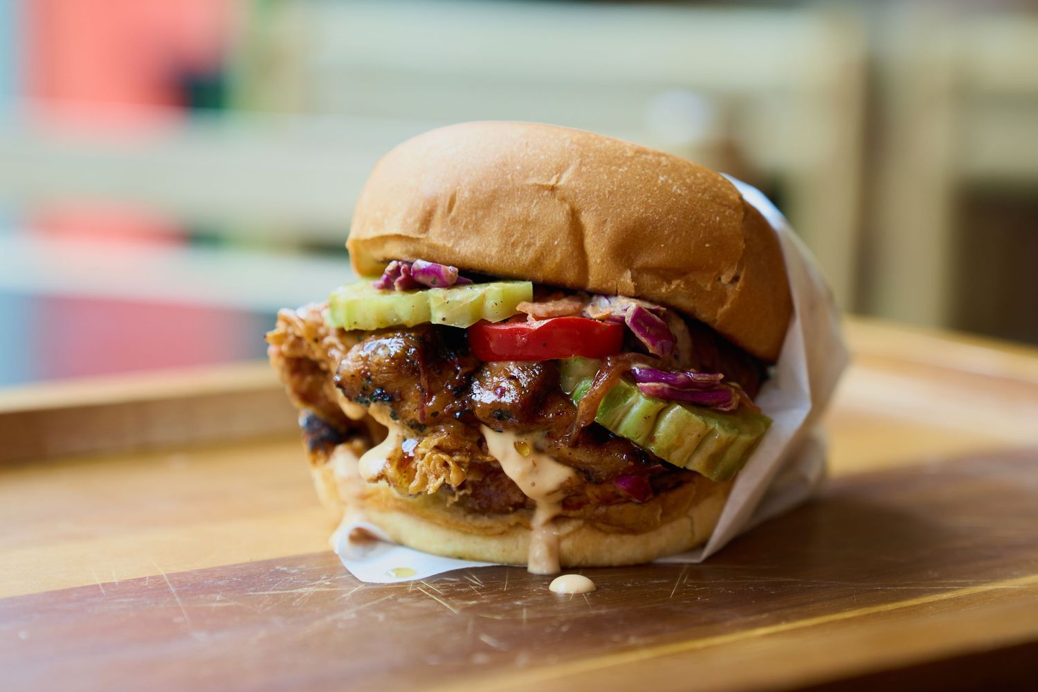 Crispy fried chicken sandwich with pickles and red cabbage slaw on a wooden board.
