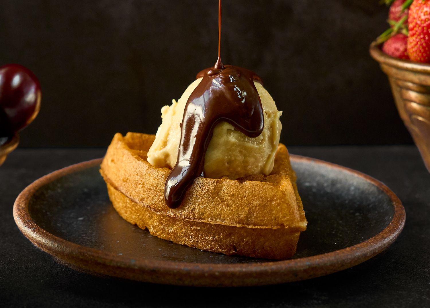 Waffle topped with vanilla ice cream and warm chocolate sauce drizzle on a ceramic plate.