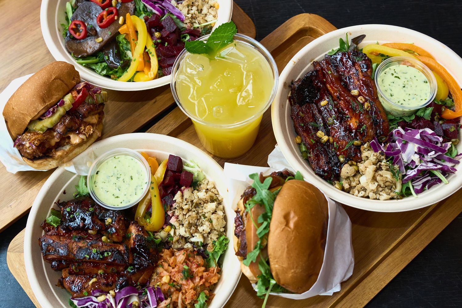 Colorful vegan bowls with grilled ribs, grain salads, burgers, and fresh juice on a tray.
