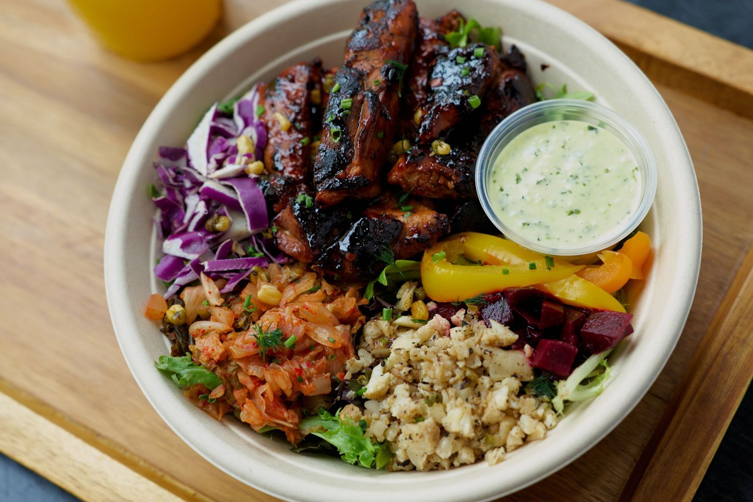 Hearty grain bowl with glazed ribs, red cabbage, peppers, rice, and green herb sauce.