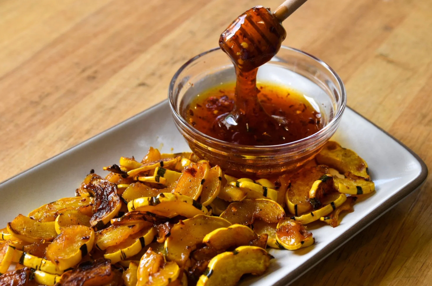 Roasted squash slices on a white platter with a glass bowl of honey and a honey dipper drizzling.