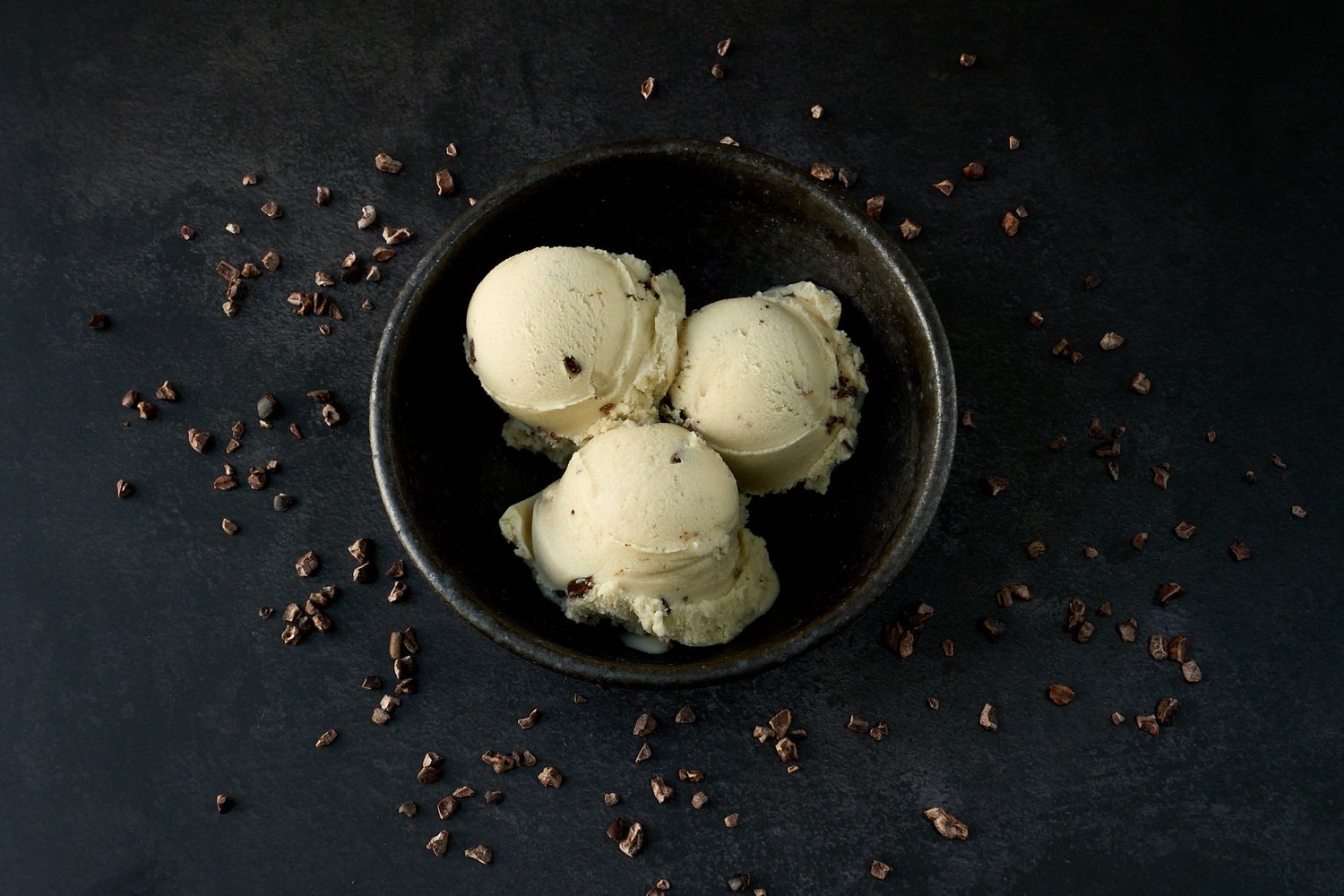 Three scoops of vanilla ice cream with chocolate chips in a dark ceramic bowl.