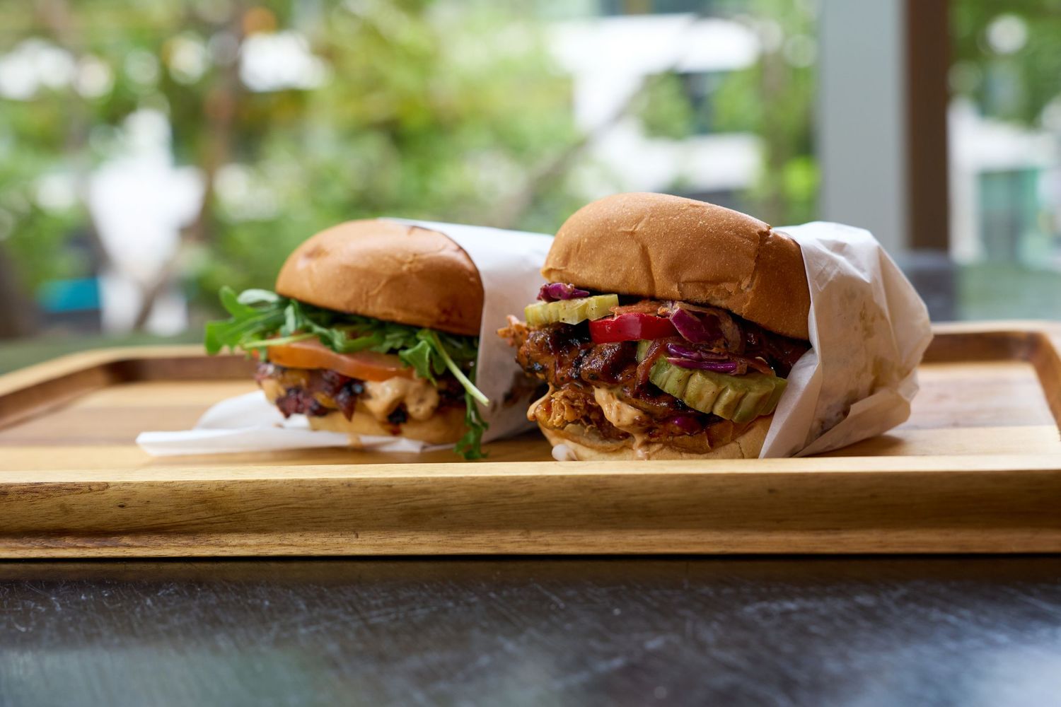 Two crispy fried chicken sandwiches with fresh toppings served on a wooden tray.