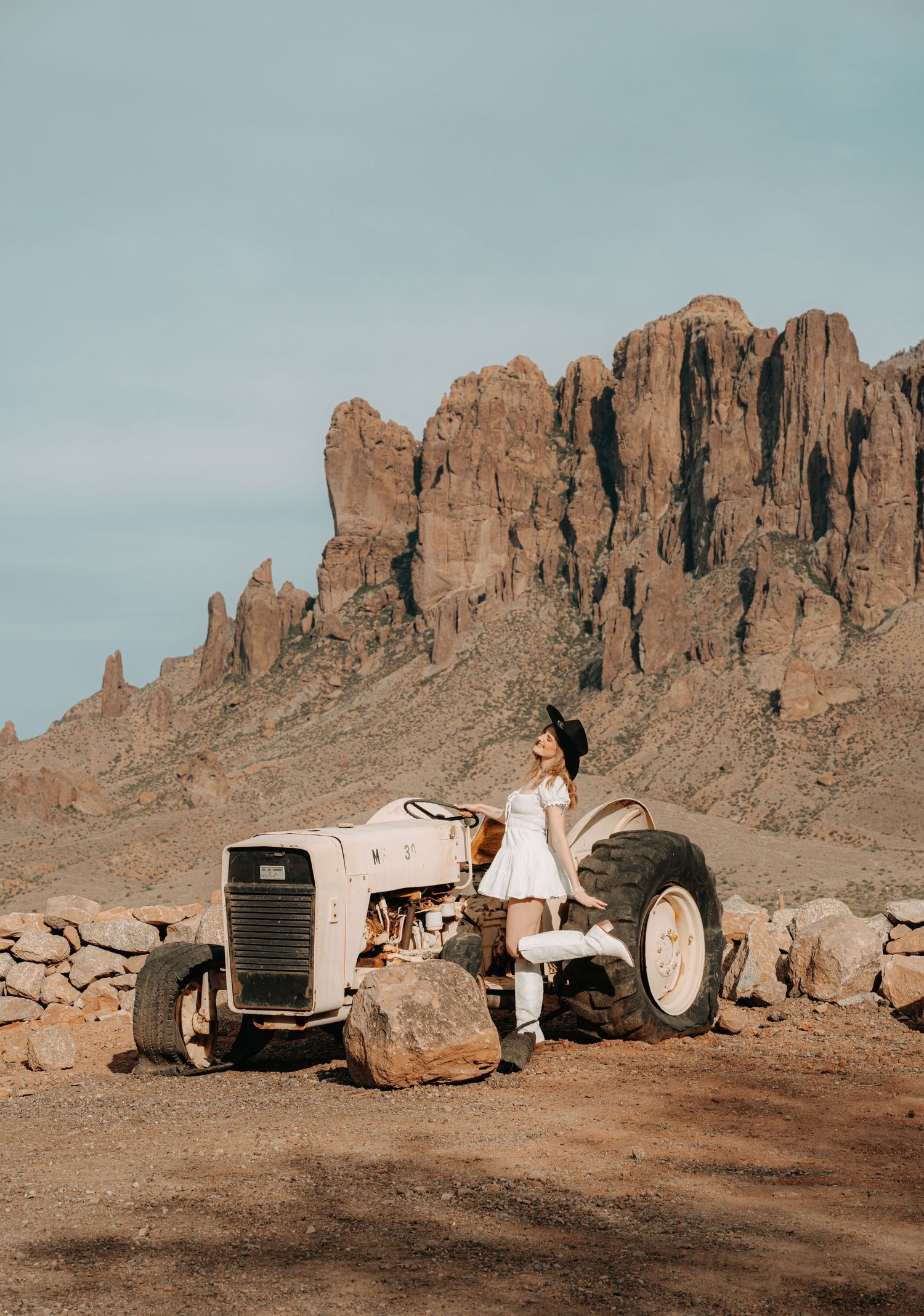 tractor photoshoot with western styles and a beautiful mountain and rocks in the background. cowboy hat and cowboy outfit