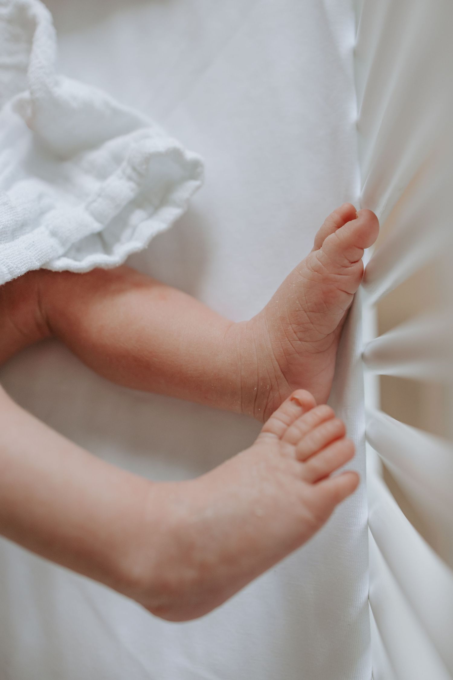 Delicate newborn baby feet and toes pressed against soft white crib fabric.