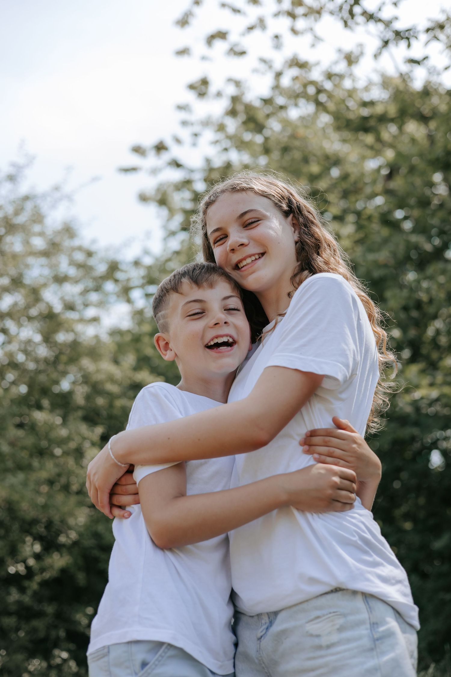 Laughing siblings hugging each other in white t-shirts in nature.