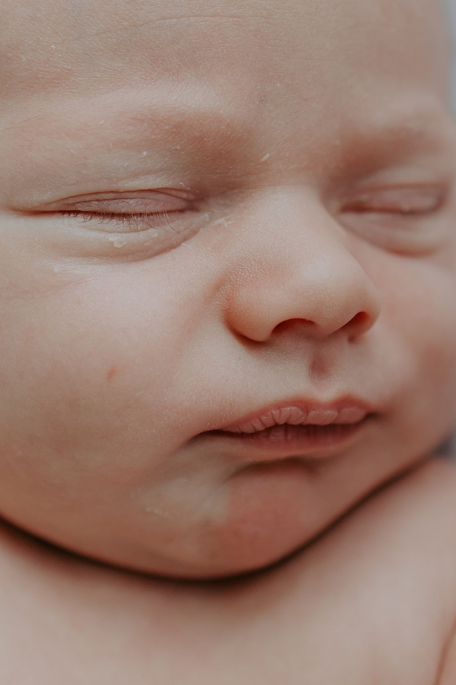 Extreme close-up of sleeping newborn baby face with delicate features and soft skin.