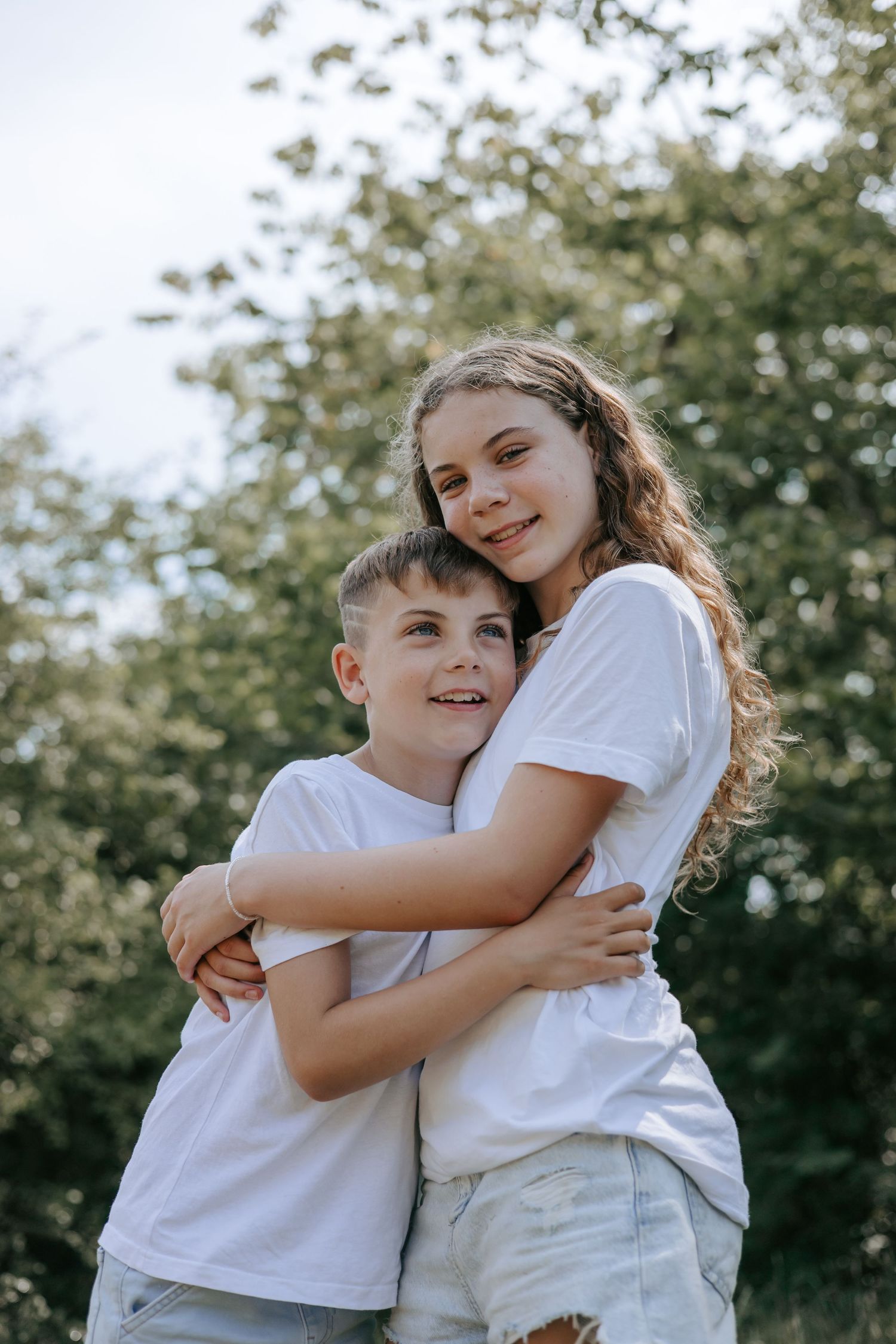 Teenage girl hugging younger brother in white t-shirts outdoors.