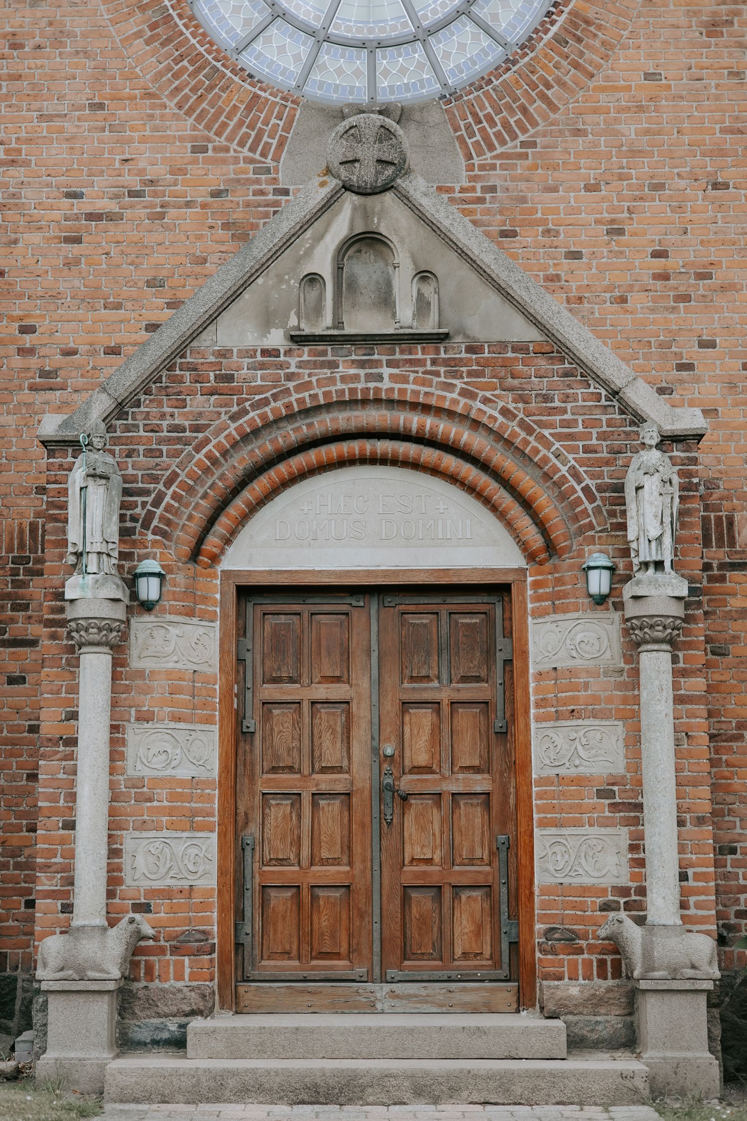 Ornate wooden double doors of a historic red brick church with stone carvings.