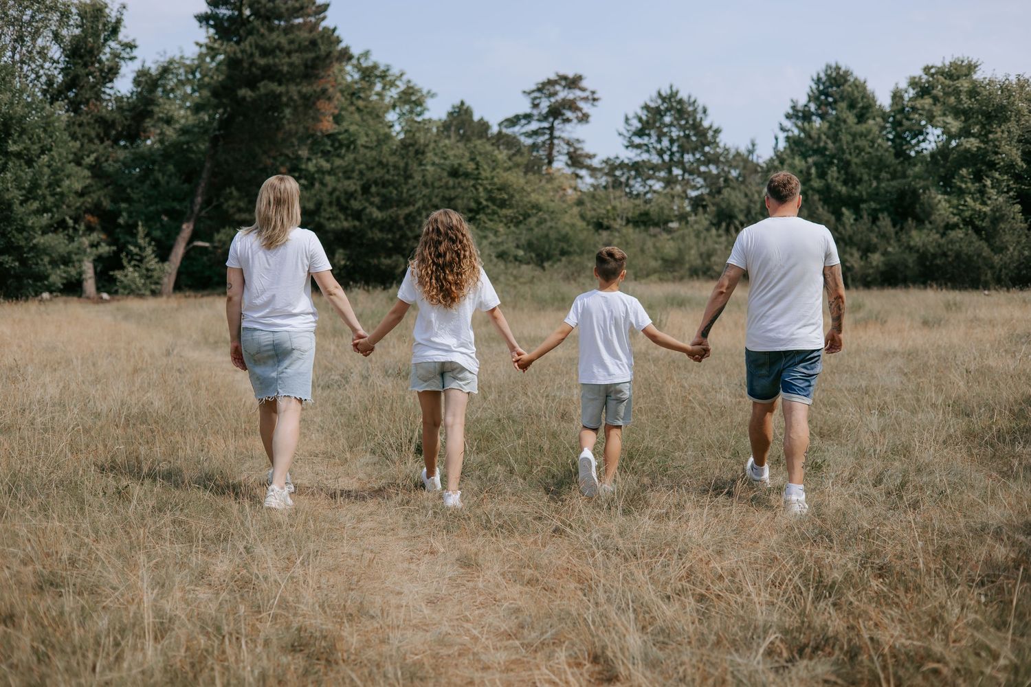 Family of four holding hands walking through an open grassy field.