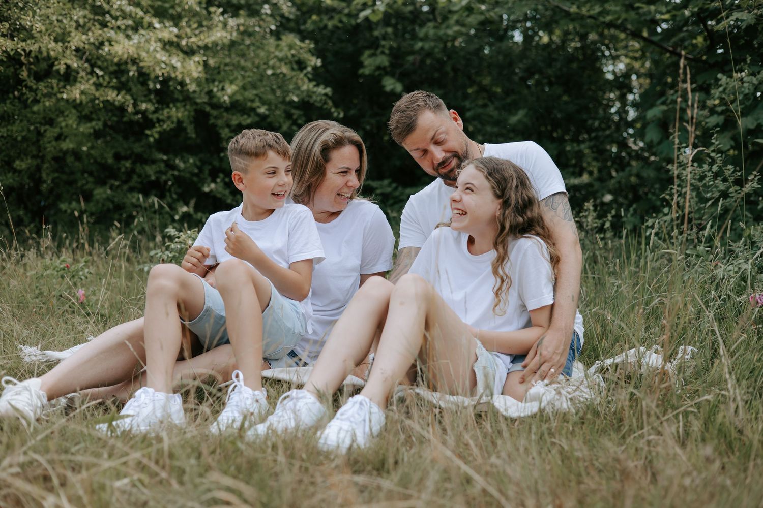 Joyful family of four sitting on a blanket in a grassy field, laughing and bonding outdoors.