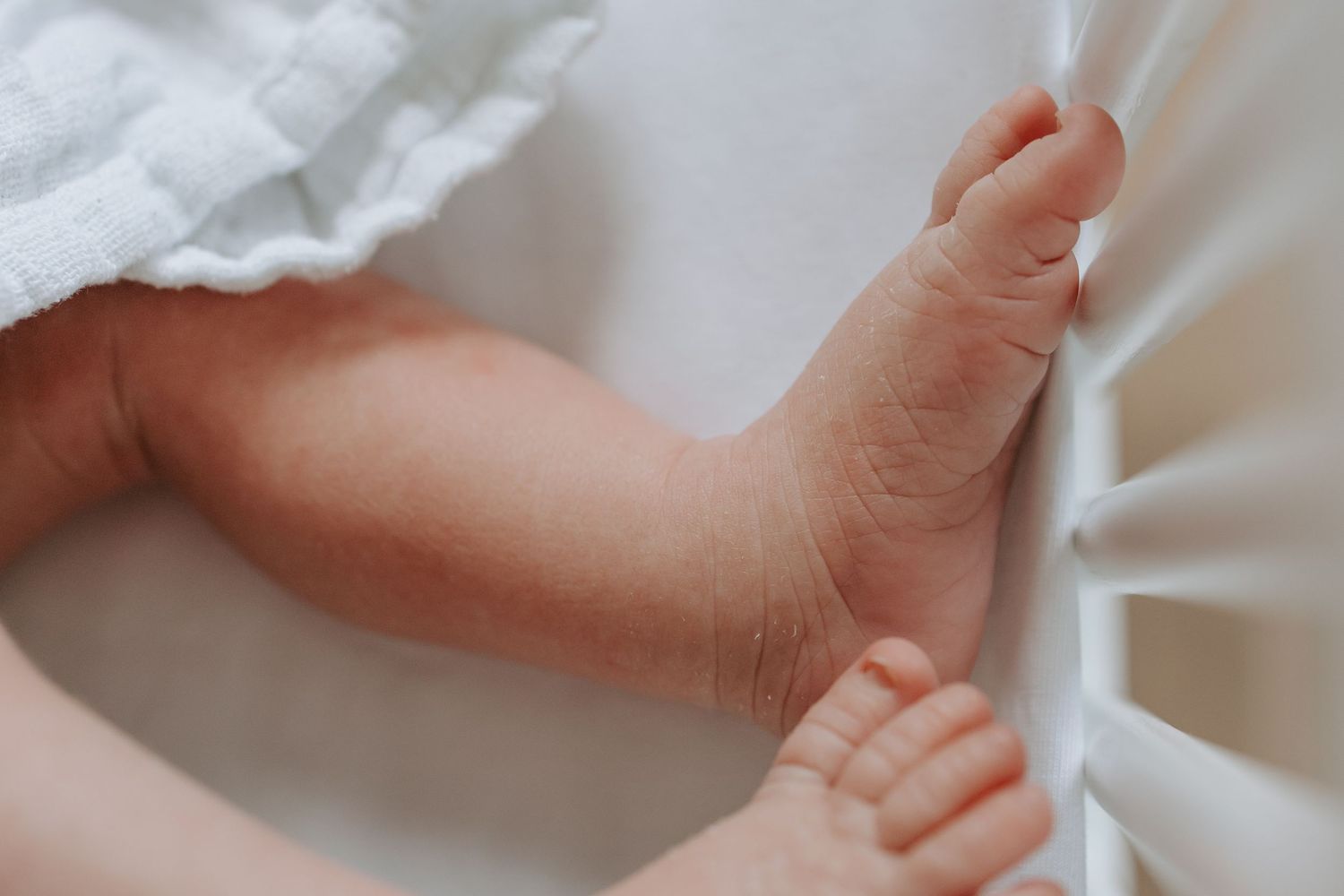 Close-up of a newborn baby's tiny feet and toes resting against white crib slats.