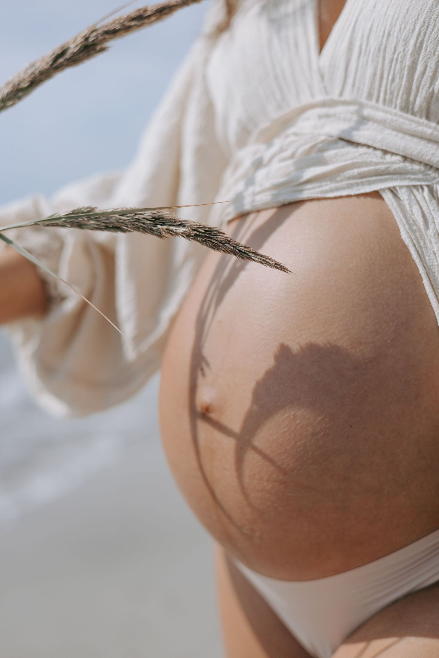 Close-up of pregnant belly with shadow of dried grass stem at the beach.