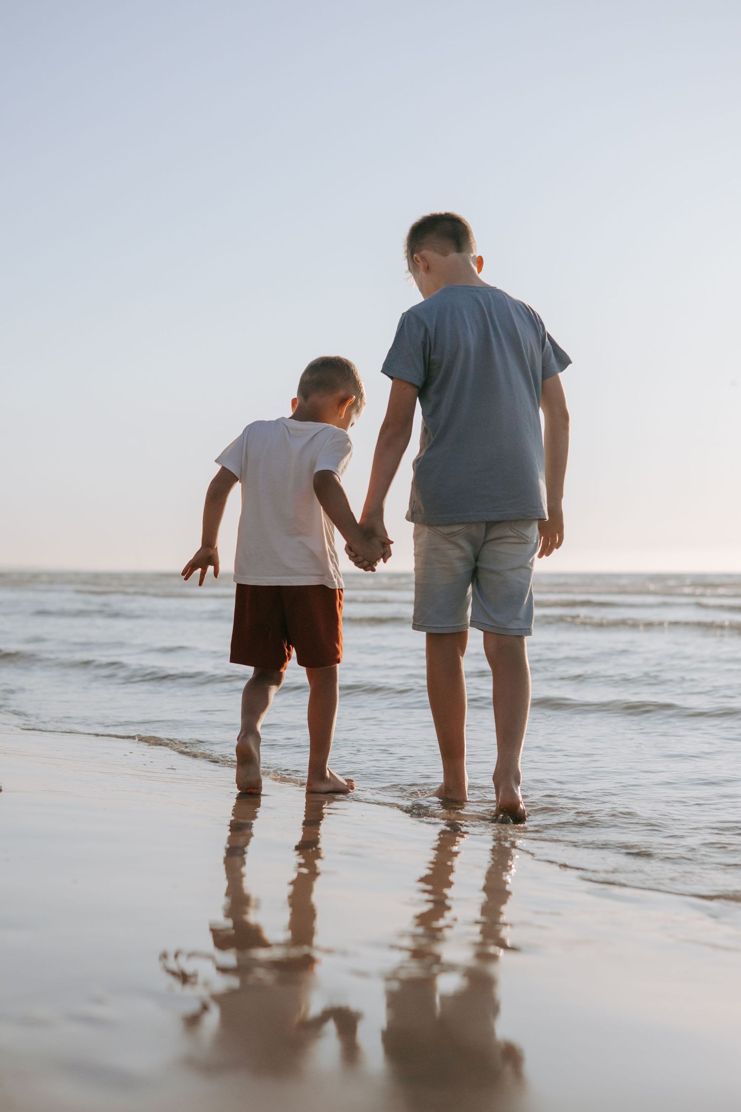 Two brothers holding hands walking along the beach at sunset.