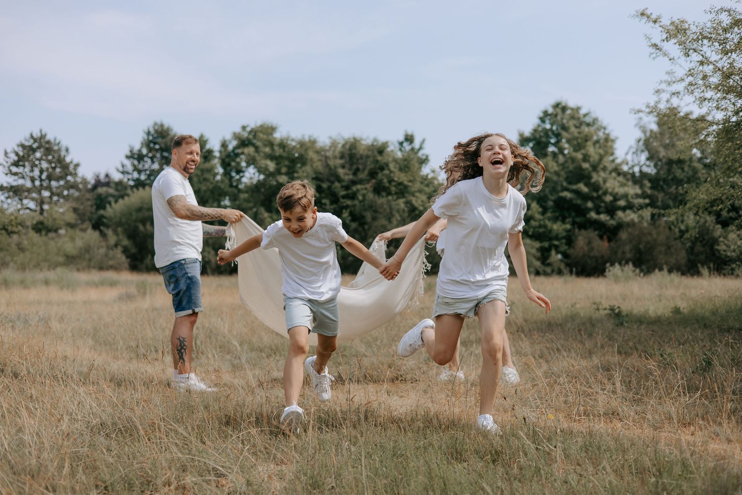Happy family running and playing together in a sunny meadow, wearing matching white outfits.
