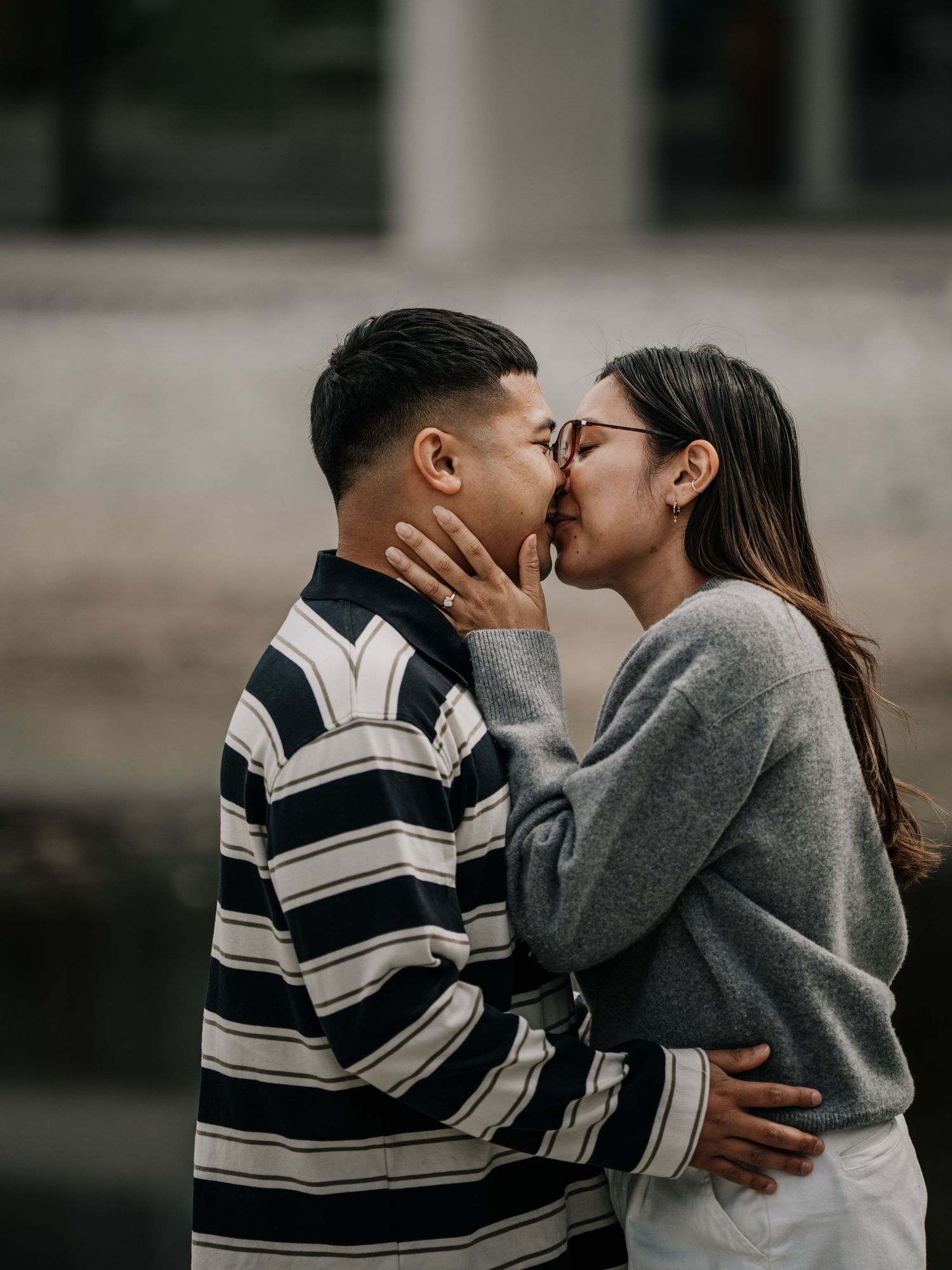 Couple sharing a romantic kiss outdoors, man in striped shirt, woman in gray sweater.