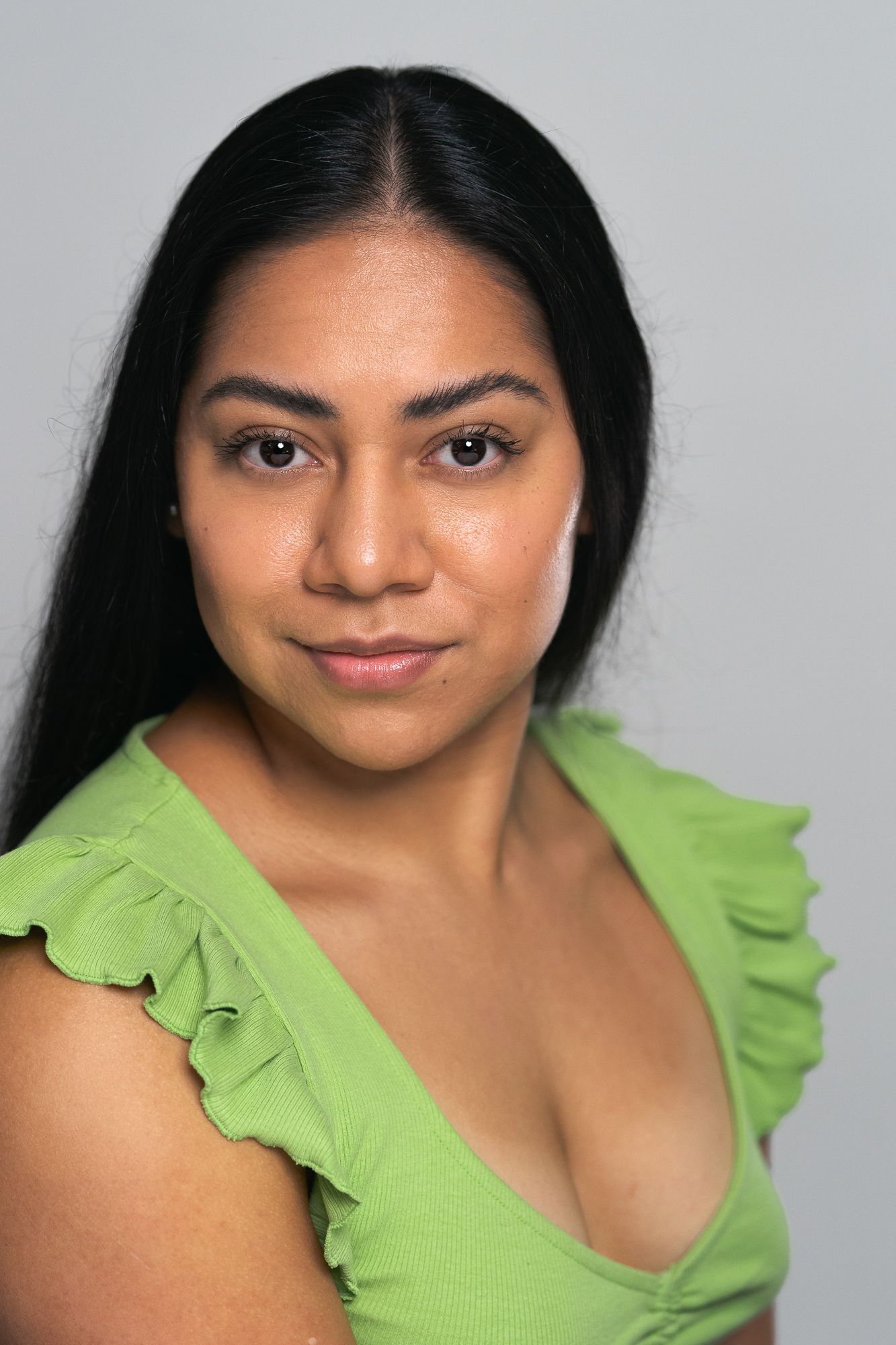 A young Latina woman with long black hair wearing a green ruffled sleeveless top poses for a headshot.