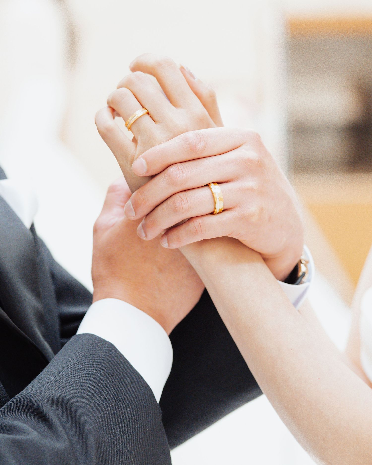 Newlywed couple holding hands showing matching gold wedding bands, symbolizing love and commitment.