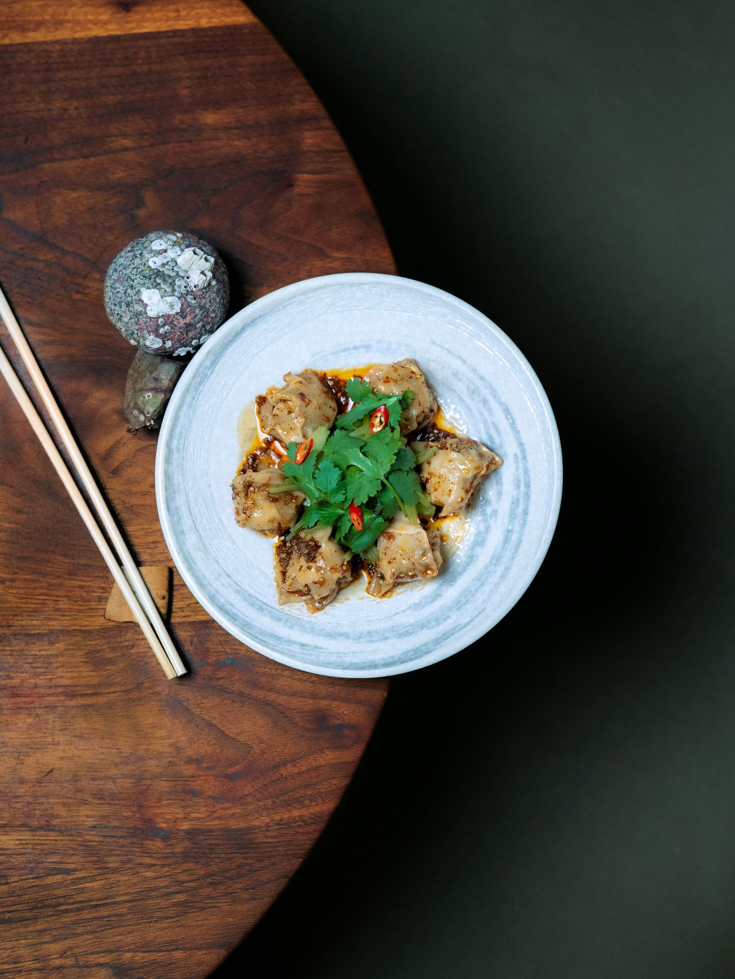 Asian dumplings in savory sauce topped with fresh cilantro served in a ceramic bowl with chopsticks on wooden table.